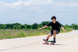A young Asian man in a black shirt and pants is playing figure skating on a rural road. in the sun on a bright day, Play surf skate