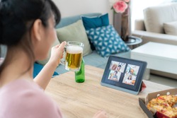 Asian woman virtual happy hour meeting party and drinking alcohol beer online together with her friend in video conference with digital tablet for a online meeting in video call 