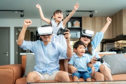 Happy Asian family at home on living room sofa having fun while they are looking mother and father playing games using virtual reality headset VR in living room at home.