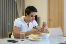 An Asian man is eating dinner alone at the dining table at night at home.