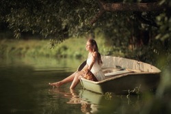 Young girl with a small dog in a boat on the lake in the rays of light