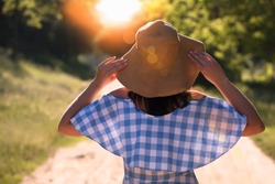 Back view of woman in a straw hat, which relaxes in the sun. Silhouette, sun lights.
