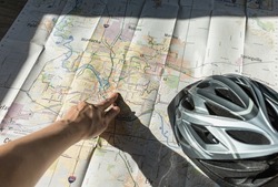 Cyclist pointing on city bike trail map, prepare for route direction around town with natural sunlight, traveling concepts. Summer outdoor activity.