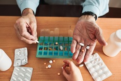 Senior man organizing his medication into pill dispenser. Senior man taking pills from box. Healthcare and old age concept with medicines. Medicaments on table