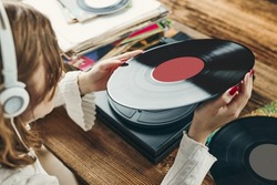 Young woman listening to music from vinyl record player. Playing music on turntable player. Female enjoying music from old record collection at home. Stack of analog vinyl records. Retro and vintage