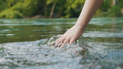 Woman hand gently touches the surface of the water in the forest river or lake.