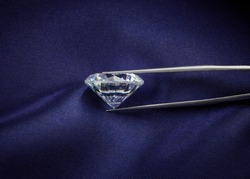 Side View of Diamond Held in Tweezers on Dark Blue Silk Background