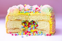 Madeira sponge coated with yellow colour frosting, layered with plum  jam, filled and topped with multicolour chocolate nibs and decorated with multicolour frostings and sugar decorations, pinata cake