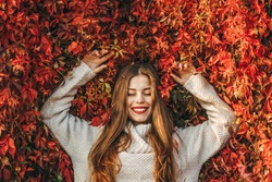 Young happy woman upon a wall of red ivy leaves.