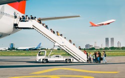 People are boarding from apron, by the stairs. Background city view.