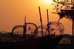 Silhouette of lobster pots or traps on fishing boats against an orange sunset sky, southeast Asia