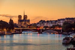 Notre Dame de Paris Cathedral, Ile Saint Louis and the Seine River at sunset. Summer evening with the Sully Bridge and city lights in the 4th Arrondissement of Paris. France