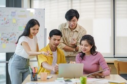 Group of young Asian business people brainstorming, looking at laptop computer.