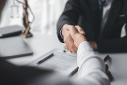 Lawyer shaking hands with a client making about documents, contracts, agreements, cooperation agreements with a female client at the lawyer's desk and a hammer at the table.