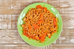 Pasta with carrots and meat in a green plate on a wooden table. Vermicelli with orange sauce on a pink shabby board. Place for text near the plate. Copy space for design.