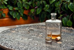 Bottle of alcohol near a glass on an empty table. The concept of alcoholism, loneliness and depression. Old vintage bottle on a wooden table. The table is wet from the rain.