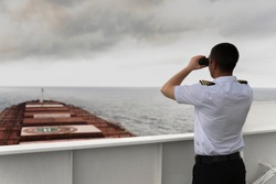 Navigator on the bridge of a large bulk carrier, doing lookout at the horizon with his binoculars

