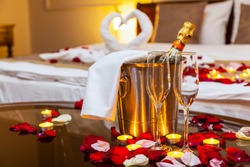 Hotel room for a honeymoon: a table with a fruit plate and candles, in the background a bed decorated with swans of towels and rose petals