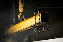 The crane moves a reinforced concrete product with holes.Reinforced concrete pillars fixed with metal hooks and chains on the background of the plant