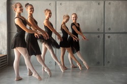 Young beautiful ballerinas in black dresses, young pantyhose and pointe shoes stand in one row and dance a ballet in the form of a black swan in a dark dance stage