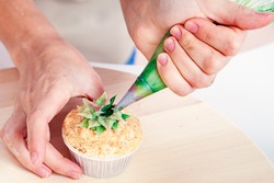 A close-up of a confectioner woman decorates using a pastry syringe and a cap made from natural products with a sweet cream of green color. Dietary Vegan Creamcakes