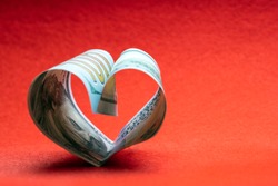 100 dollars. A hundred dollar bill folded in the shape of a heart on a red background. Copy space. Concept of money, love and a gift for Valentine's Day.