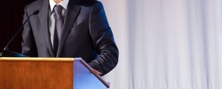 Speech of an abstract man in a suit on stage at the stand for performances. Tribune or pulpit for speaker official, president or professor. Close-up. Copy space.
