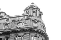 The top front corner of an old  rounded sandstone building. Domed roof with columns and arched windows. Black and white.