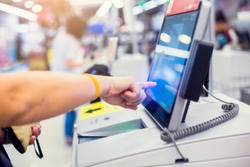 Payment blurry background image. Hand of woman customer is pressing the screen of the automatic payment machine. Self service machine in modern supermarket, self-service paypoint tills in hypermarket.