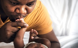 An African American father kissing foot, his 12-day-old baby newborn, with love and happy, concept to African American family and baby black skin newborn