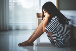 Asian woman, 23 year old, sitting near a white bed in her bedroom, She is having sadness and stress from work And health problems, to people and heartbroken concept.