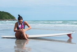 Asian women sitting on the beach she has a knee injury after working out by surfing in the sea. to people health care and surfboard concept.