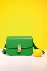 stylish little green purse or handbag on yellow background with a lemon nearby. Product composition photography. bag and reticule for women.