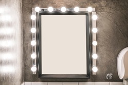 Blank makeup mirror with light bulbs on a concrete wall in a toilet