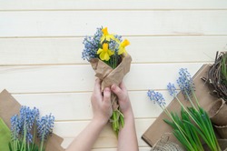 Children's hands collect a bouquet as a gift. A gift for mom. Spring festive bouquet in a crafting package. Pruning flowers. The child is a florist. Wooden background. Field bouquet. Eco-style.