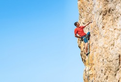 Athletic man climbs an overhanging rock with rope, lead climbing. Sport climbing outdoor.
