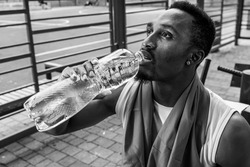 black and white photo, young muscular build man drinking water bottle after running, attractive athlete resting after outdoor workout, fitness and healthy lifestyle concept.