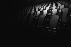 black and white photo, empty cinema. The red and black armchairs in the cinema hall are illuminated by a beam of light, a low key. Selective focus. Quarantine, restrictive tape on chairs 