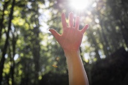 Faceless picture, man's hand covering sunlight,l sun shiing through hand, image of human's hand covering sun, bright rays of sun, isolated over park or forest background. Nature concept.