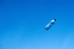 Flying bottle of water against blue sky. Background with copy space. Refreshment concept photo.