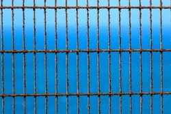 Close up of a rusted metal fence against a blue sky. Rusted metal bars in a grid pattern set against a clear, bright blue sky
