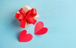A pair of red paper hearts and a gift box on a blue background.