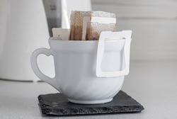 a cup of brewed natural coffee in a drip bag on the background of a teapott close-up