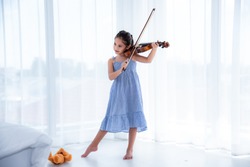 A cute white Asian girl wearing a blue skirt dress is playing a violin in a white background with sunlight.