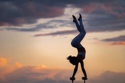 Silhouette of flexible and fit girl doing handstand and keeping balance against dramatic unset. Concept of yoga and healthy lifestyle 