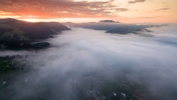 Aerial View: Sunrise over hillside as the sun rising from horizon reflect light bright yellow sky. Below cloudy mist covered valleys flooded pine forests create impressive beauty highlands in morning.
