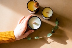 wooden wick candles. Handmade candle from paraffin and soy wax in glass with leaf on craft background. Let flay. Candle making. Top view. Womans hands holding the candles