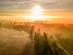 drone photo of foggy sunrise over forest, lake an village in North Sweden - golden sun light with beams and shadows. Västerbotten,  West Bothnia province, north of Sweden
