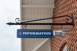 The exterior of a red and brown brick building with a white overhang. There's a black metal sign holder attached over a window. The directional sign is a blue pointing hand with the word information. 
