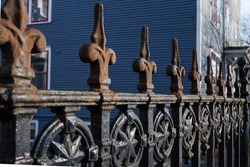 An artistic vintage rusty wrought iron fence with circular decorative symbols in between the rungs. There's a royal blue wooden building in the background. The ironwork has a star in the center.